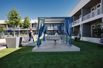 A patio with a swing set and a bench in front of an apartment building